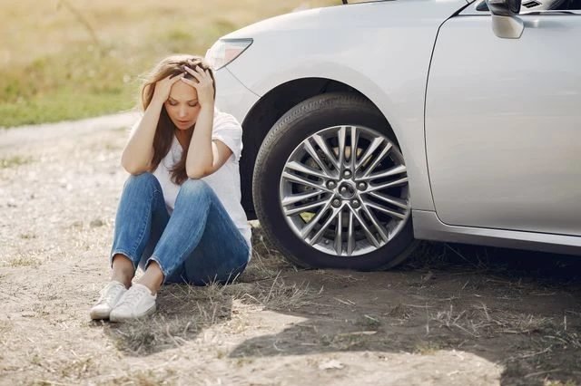 A driver sitting beside a car at the roadside after a collision.