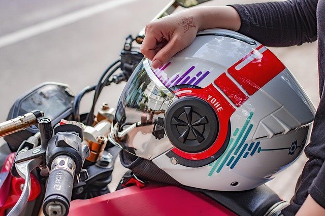 A rider holding a helmet beside the motorcycle handlebars.
